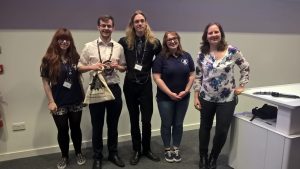 Fraser Baird (second from left) smiling with the committee of CAPS 2016 as he receives his prize - a ScienceGrrl goody bag - from Director Dr Heather Williams (far right)